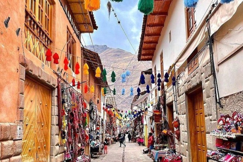 A narrow street with colorful hanging decorations, stone buildings, and a mountain in the background. 4
