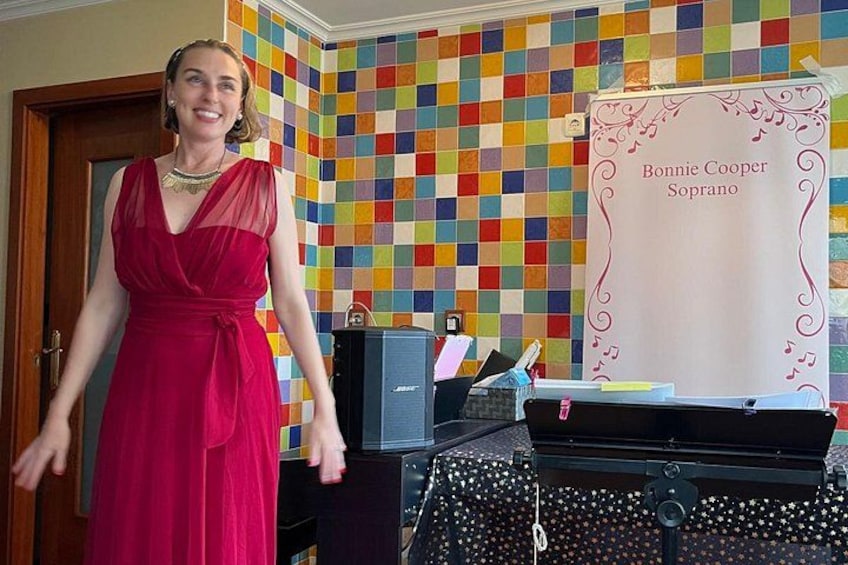 En kvinde i en rød kjole står foran en farverig ternet væg og et skilt med teksten 'Bonnie Cooper Soprano'. 5