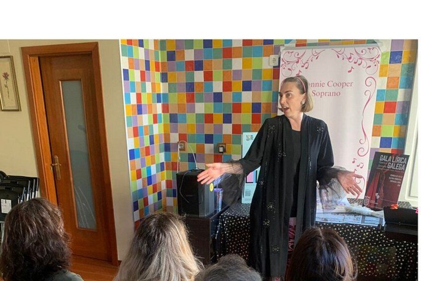 En person taler ved et arrangement med en farverig baggrund og et banner med teksten 'GALA LIRICA BALEGA'. 3