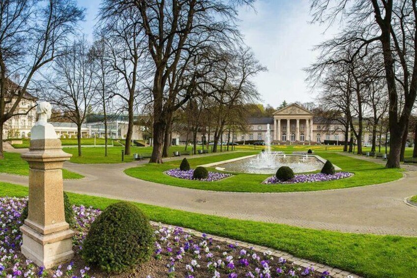 A park with a fountain, manicured lawns, a statue, and a classical building in the background. 2