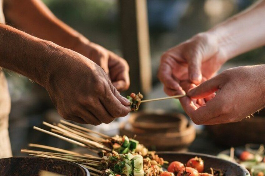 Hands holding skewers with food, a bowl of sauce, and a pot in the background. 4