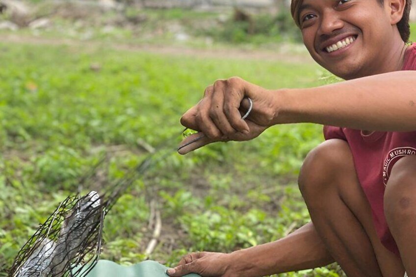 A person crouching outdoors, holding a tool near a wire mesh. 5