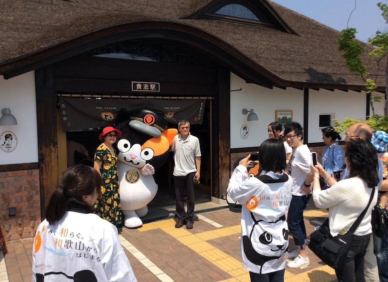 A building entrance with a sign, a mascot, and people taking photos. 1