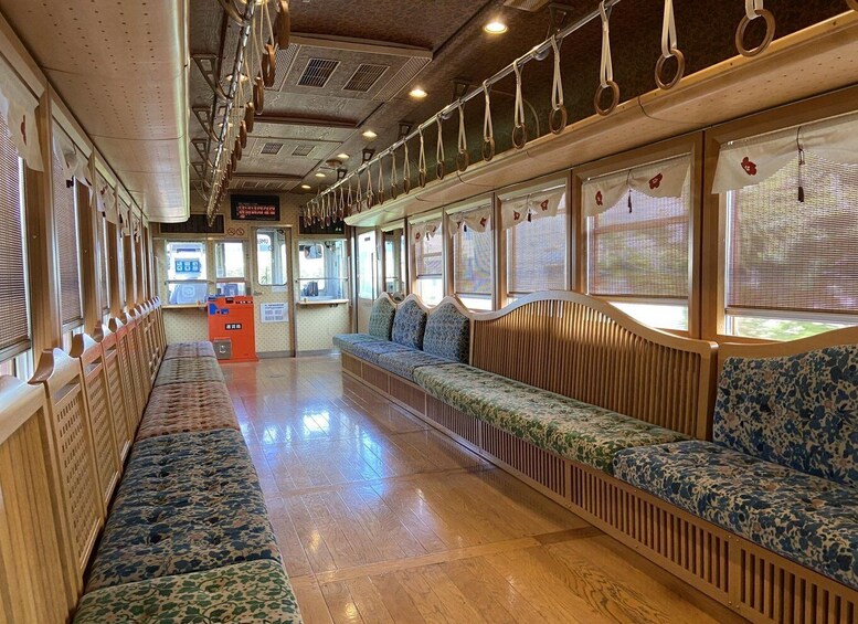 A train carriage interior with wooden benches, patterned upholstery, and a ticket machine. 2