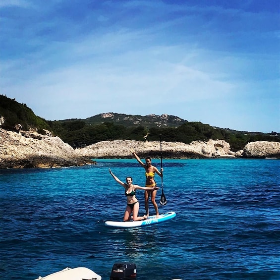 Two people paddleboarding on a calm sea with clear skies and rocky hills in the background. 5