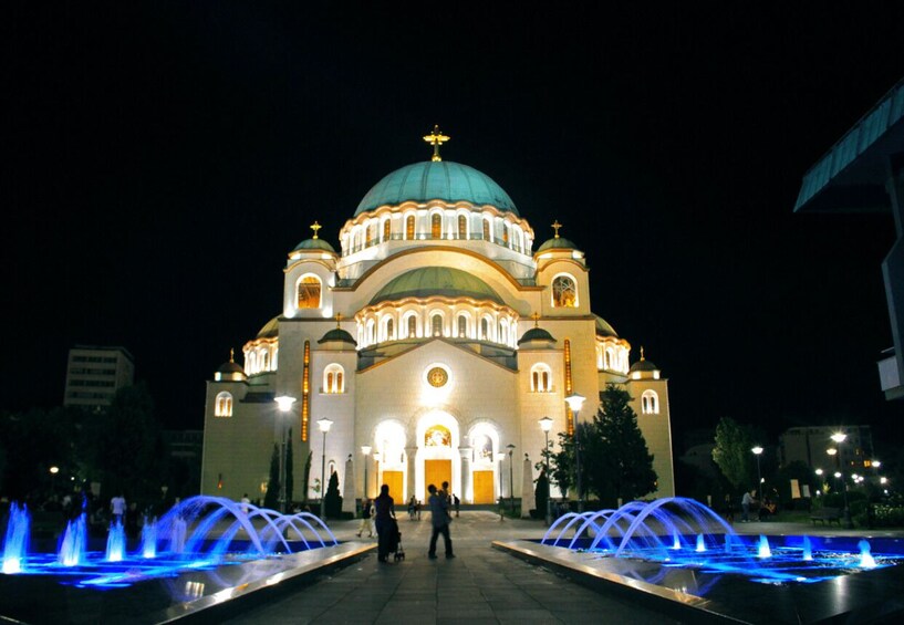 A large, illuminated church with a dome and two towers, surrounded by a fountain with blue lights. 5