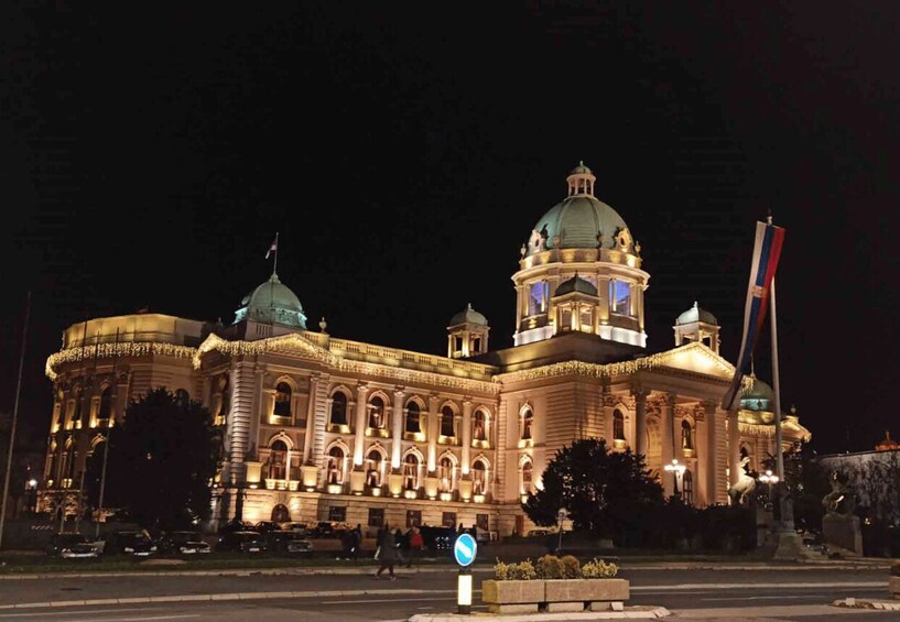 A grand, illuminated building with a large dome and multiple smaller domes, surrounded by a well-maintained garden and a flagpole. 2