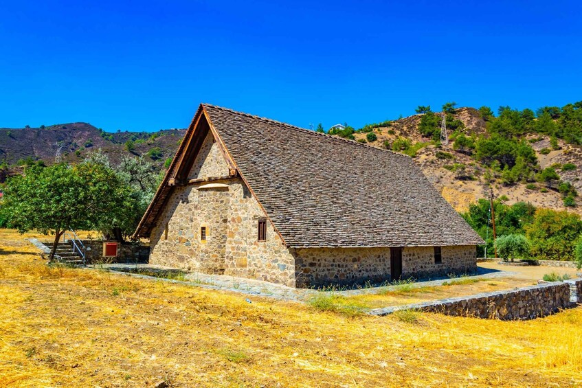 A stone building with a sloped roof, surrounded by dry grass and a hillside. 1