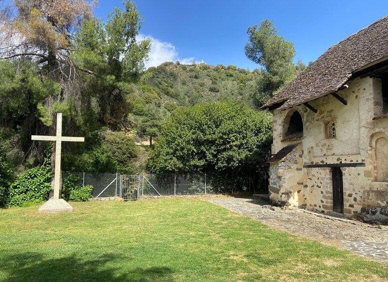 A church with a cross in front, surrounded by greenery and a stone building. 4