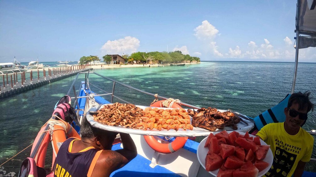 A boat with a person holding a plate of food, another person with a life jacket, and a pier with boats in the background. 4