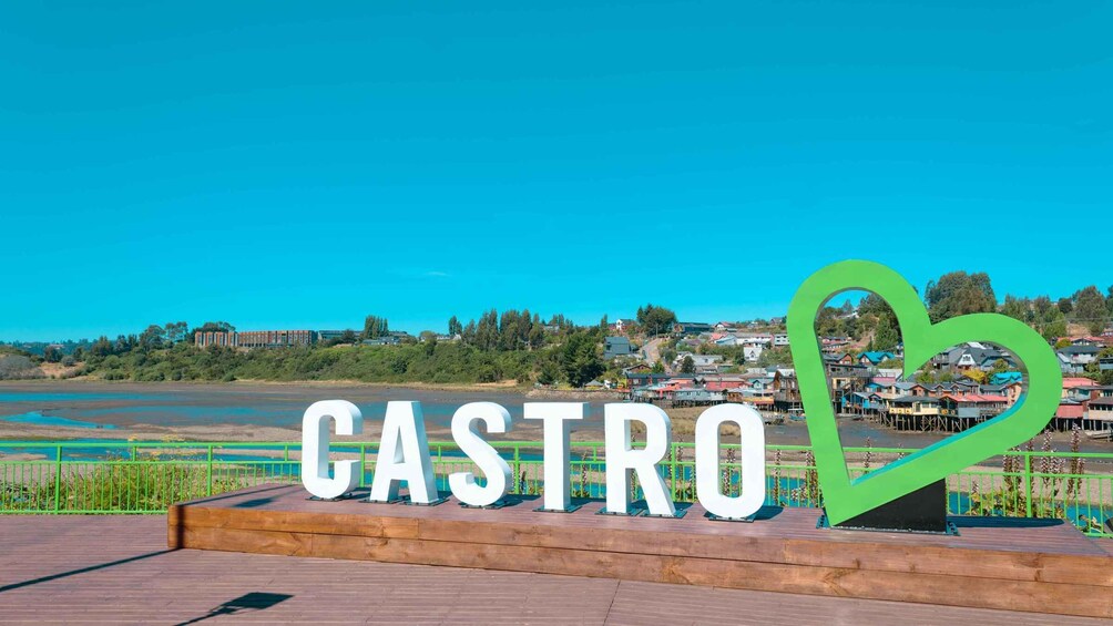 A sign with the word 'CASTRO' and a heart symbol, with a scenic view of a town and a river in the background. 5