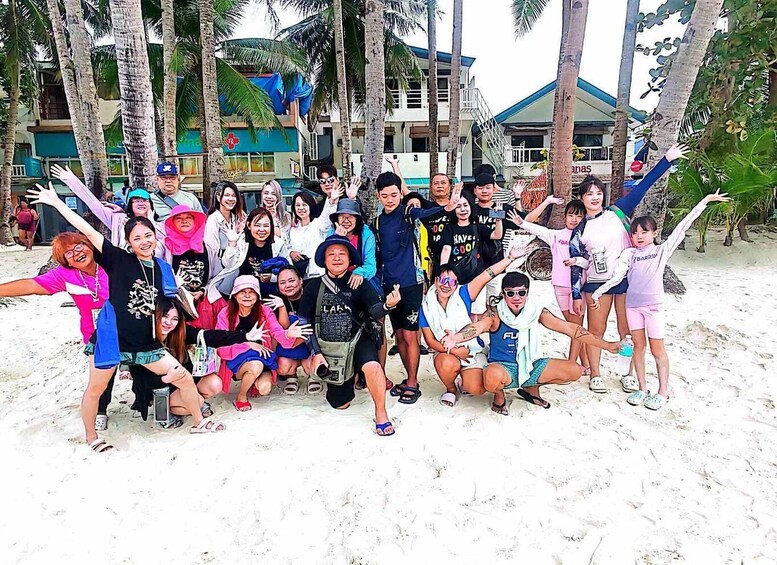 A group of people posing on a sandy beach with palm trees and buildings in the background. 5