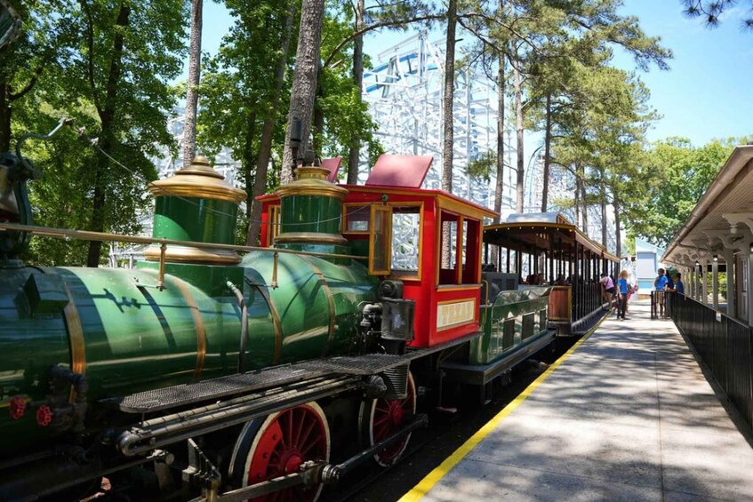 A green and red vintage train on tracks, surrounded by trees and a clear sky. 4