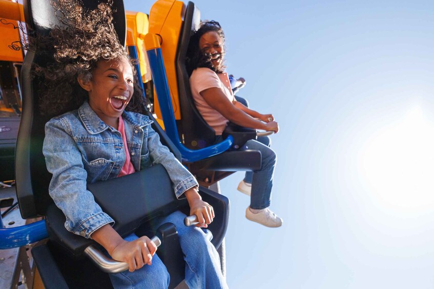 Two people seated on a roller coaster, holding onto the safety bars. 1