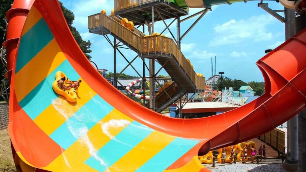 A water slide with a colorful design, a wooden platform, and a roller coaster in the background. 2