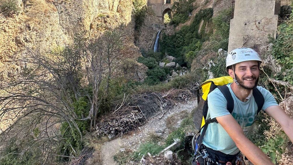 A hiker with a backpack on a trail surrounded by trees and a waterfall. 5