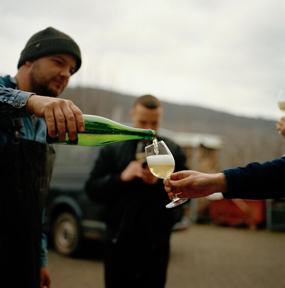 A person pouring a white liquid from a green bottle into a glass held by another person. 1