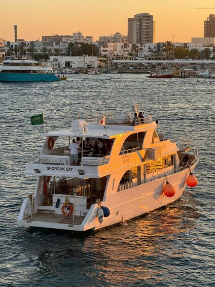 A white boat named SHOROUK SAT on the water with a city skyline in the background. 1