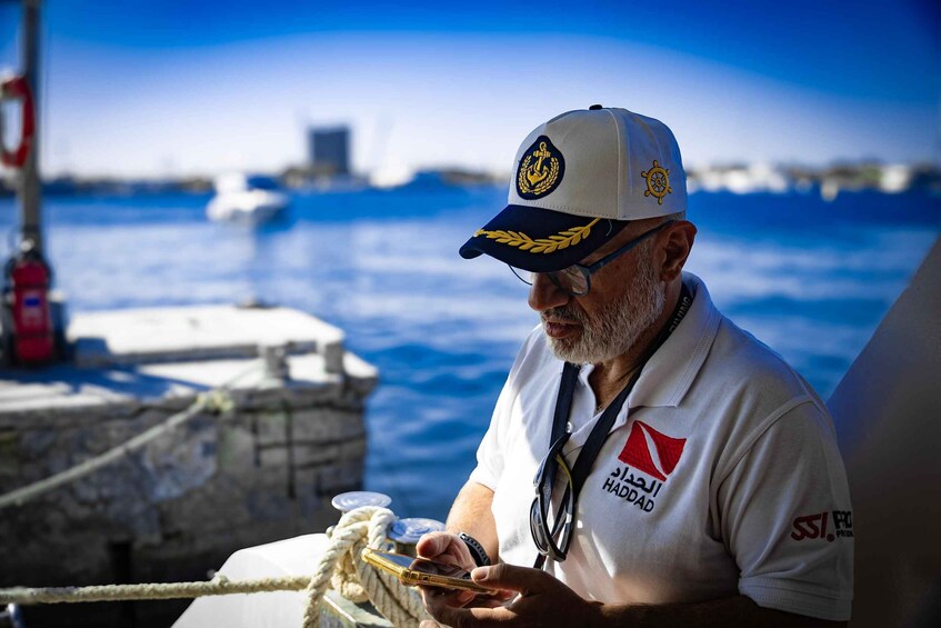 A man wearing a white shirt and a cap with a logo, holding a device. 4