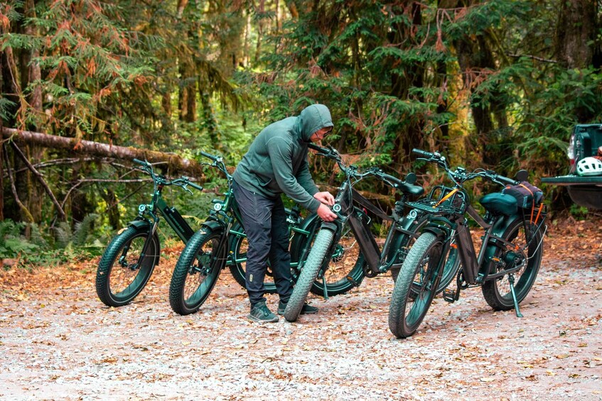 A person adjusting a green mountain bike in a forested area with leaf-covered ground. 2