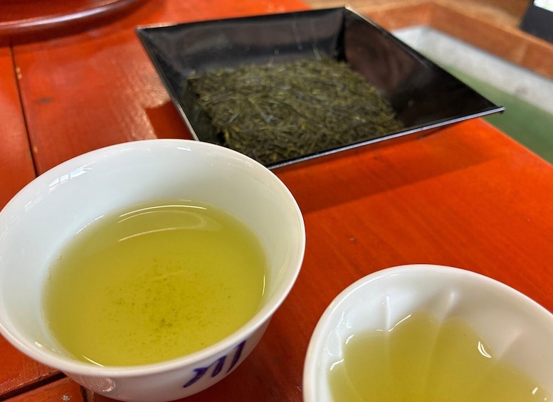 Two white bowls with yellow liquid, one with a blue pattern, and a black tray with green leaves. 5