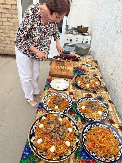 A person serving food from large bowls on a table with a floral tablecloth. 3
