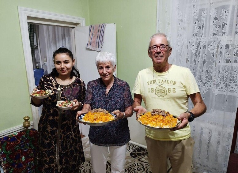 Three people holding plates of food in a room with patterned curtains and a door. 1