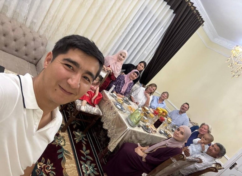 A group of people seated at a table with food and drinks, in a room with a chandelier and curtains. 1