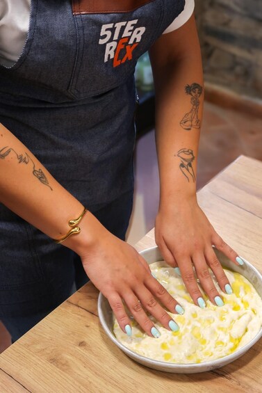 A person wearing a dark blue apron with 'STER REX' printed on it, preparing food with a bowl of yellow mixture on a wooden table. 5