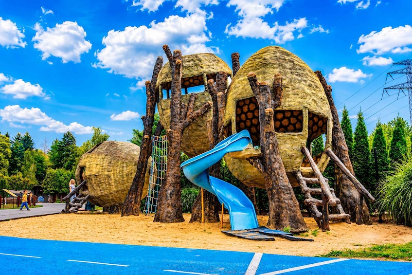 A playground with treehouse structures, a blue slide, and a sandy ground. 3