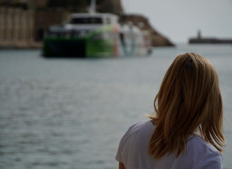 A person with long hair facing a body of water with a boat in the distance. 5