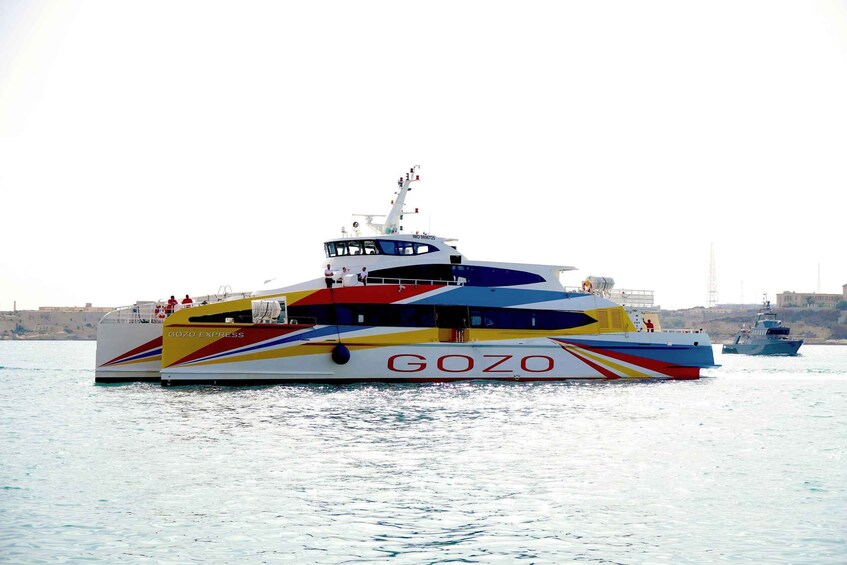 A colorful GOZO EXPRESS boat on the water with a cityscape in the background. 1