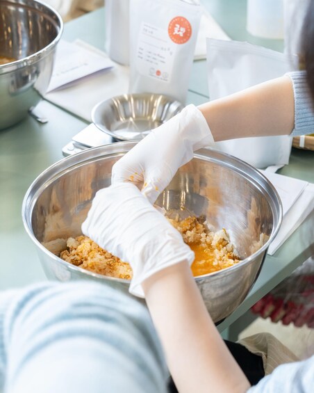 A person wearing gloves mixing ingredients in a metal bowl. 3