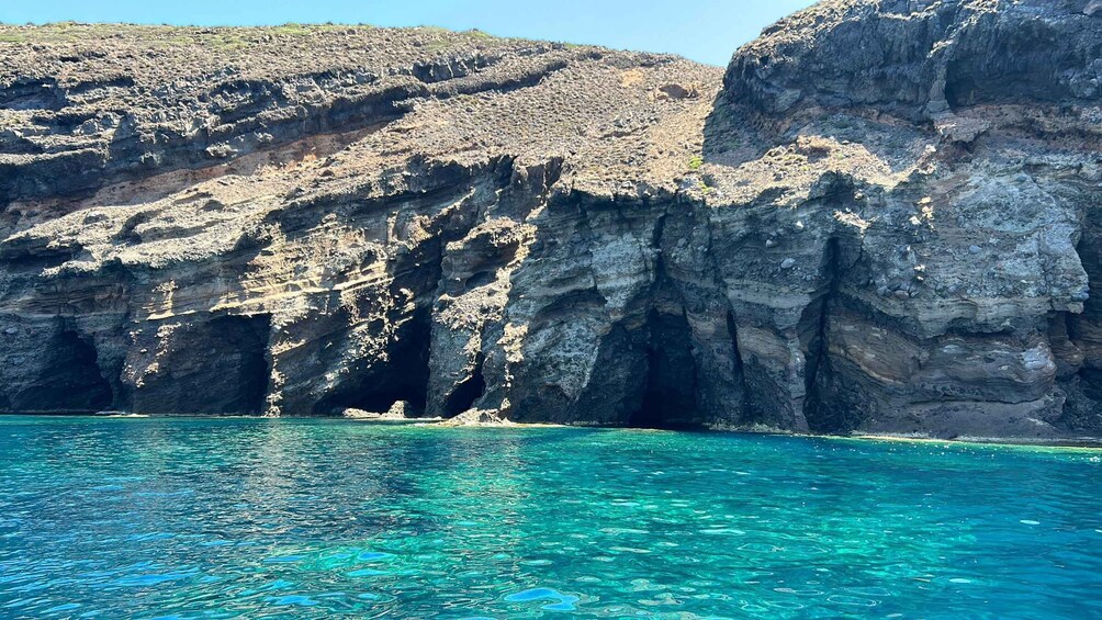 A coastal landscape with clear turquoise waters, rocky cliffs, and a rugged terrain. 1