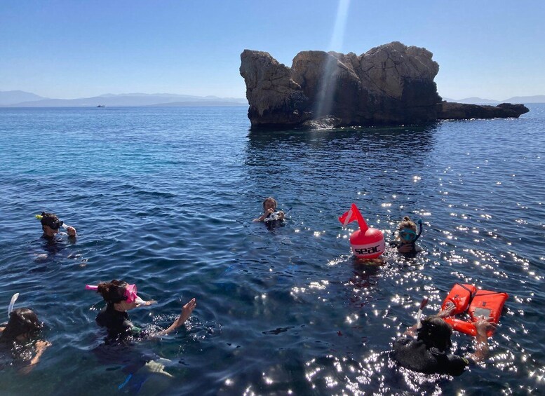 People snorkeling in clear blue water with a rocky outcrop in the background. 3