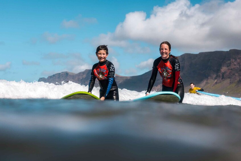Two people in wetsuits on surfboards at the beach with mountains in the background. 2