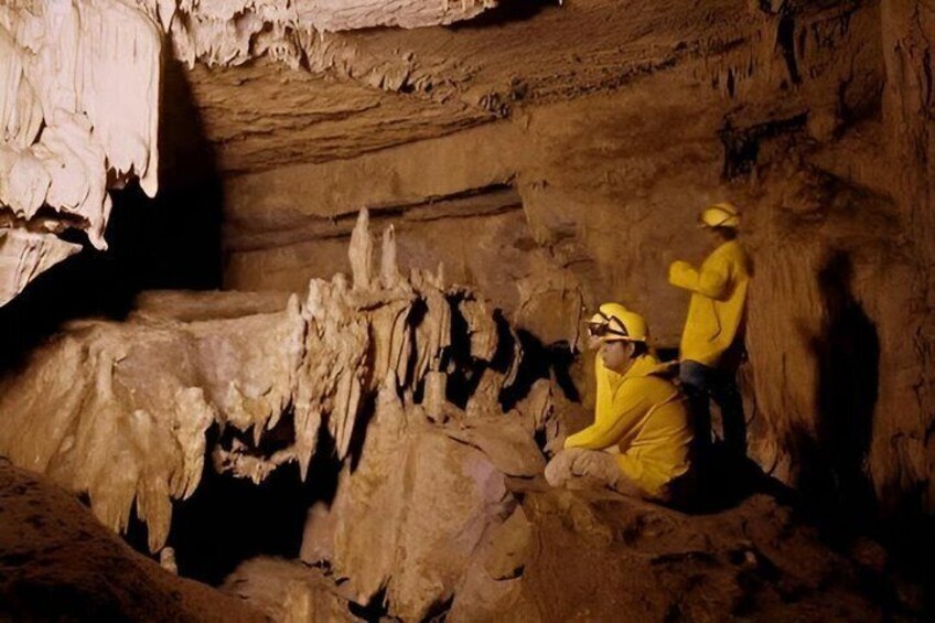 Two people in yellow protective suits and helmets inside a cave with stalactites. 3
