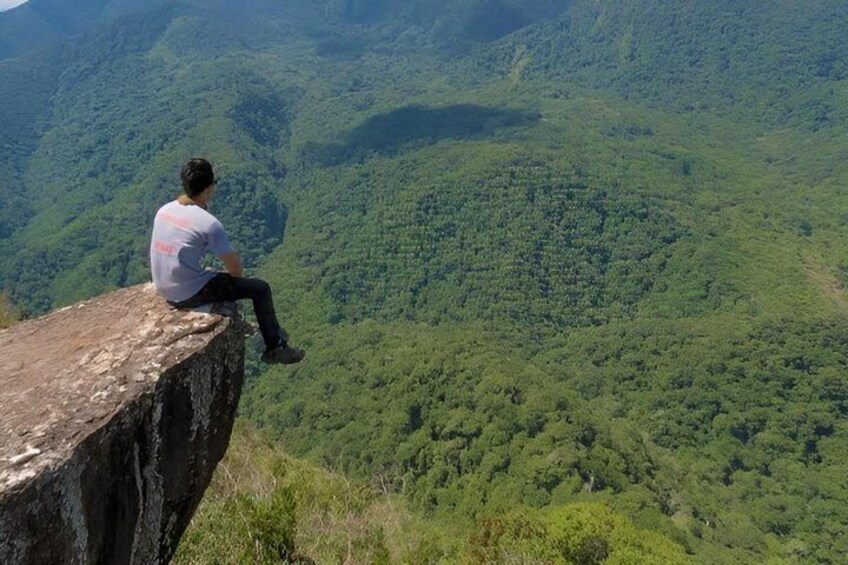 A person sitting on a cliff edge overlooking a dense forested valley. 5
