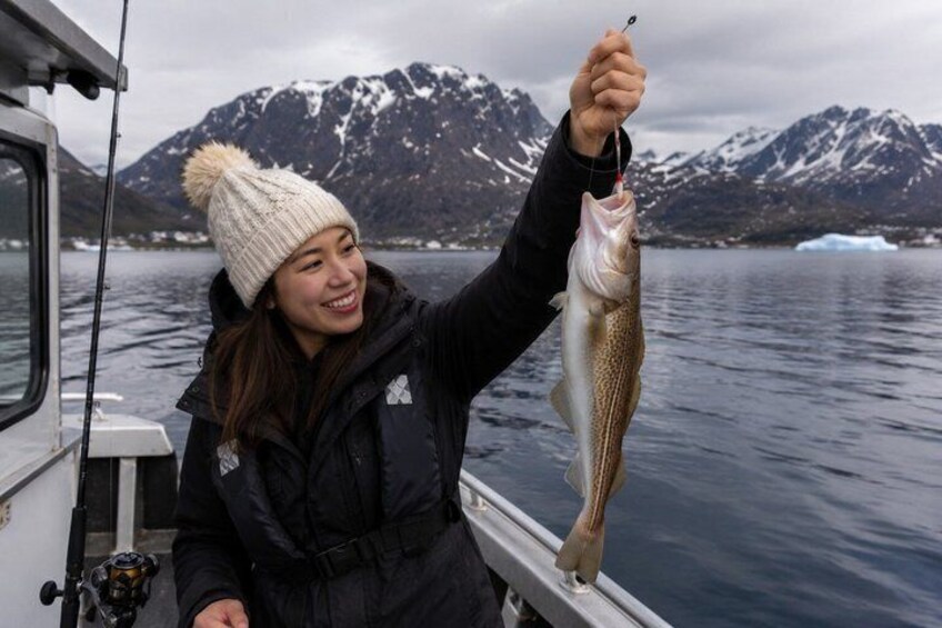A person holding a fish on a boat with a mountainous landscape in the background. 1