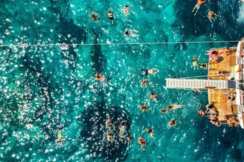 A wooden dock extending into a turquoise sea with people swimming and sunbathing. 2