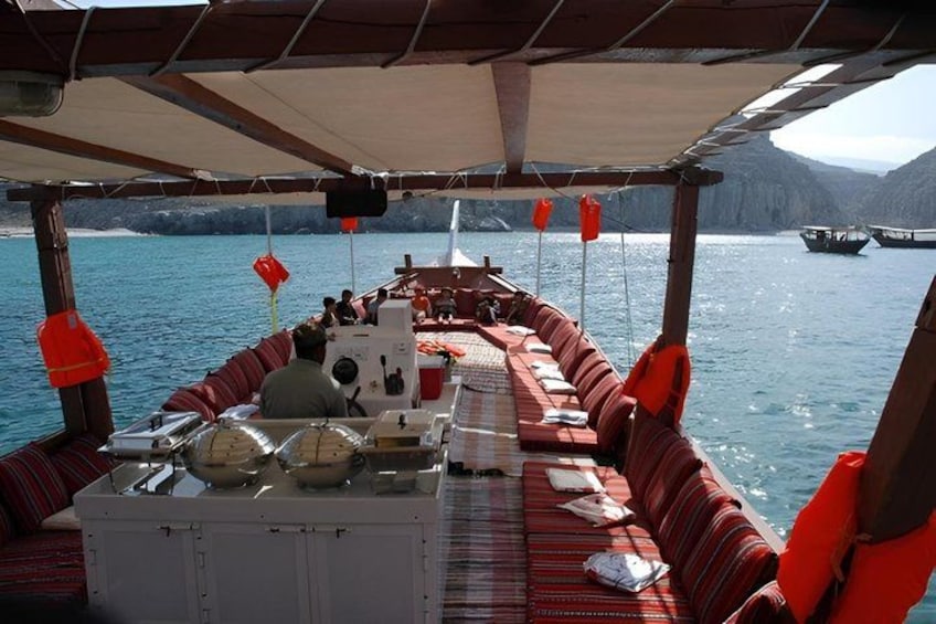 A boat with red cushioned seating, a table with food containers, and a view of the sea and distant boats. 3