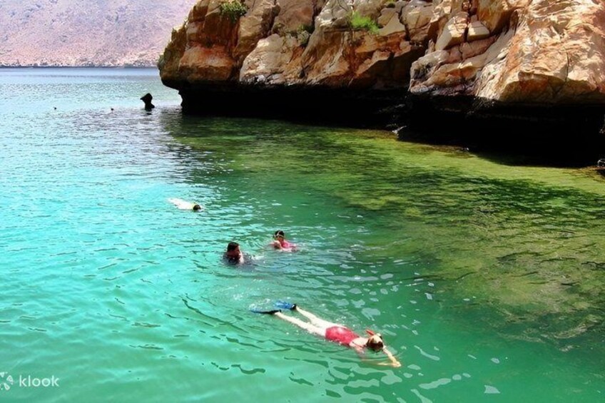 People swimming in clear turquoise water near rocky cliffs. 4
