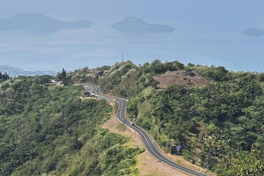 A winding road through a hilly landscape with dense vegetation and a view of the ocean in the distance. 3
