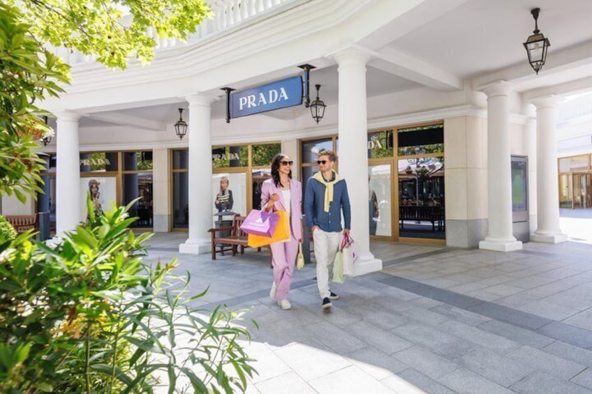 A couple walking in front of a Prada store with columns and a sign. 5