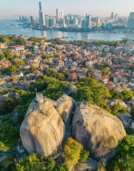 A cityscape with a prominent rock formation in the foreground and a dense urban area in the background. 3
