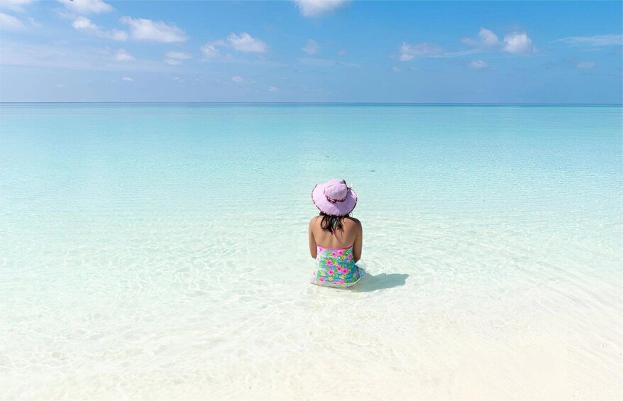 A person sitting on a sandy beach facing the ocean. 4