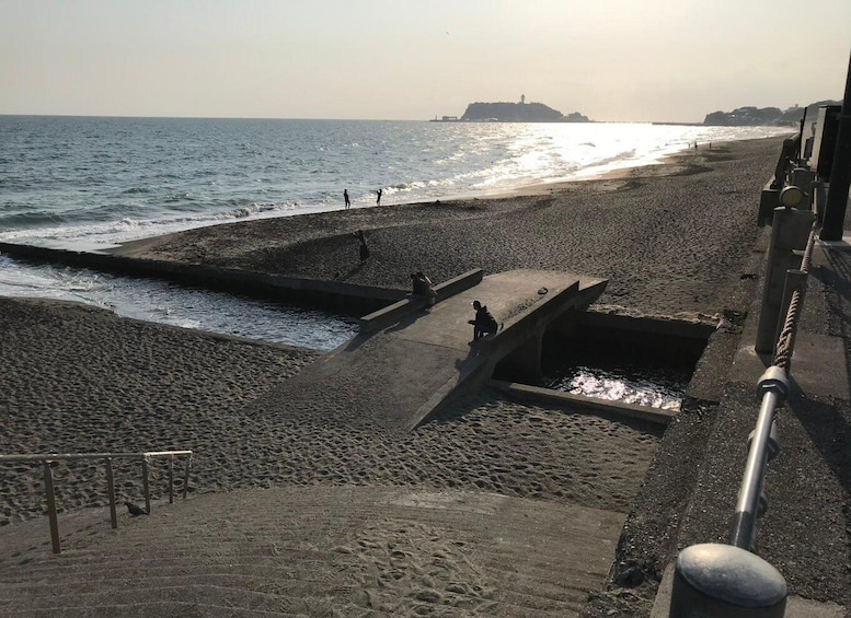 A beach with a concrete structure, people walking, and a distant island. 3