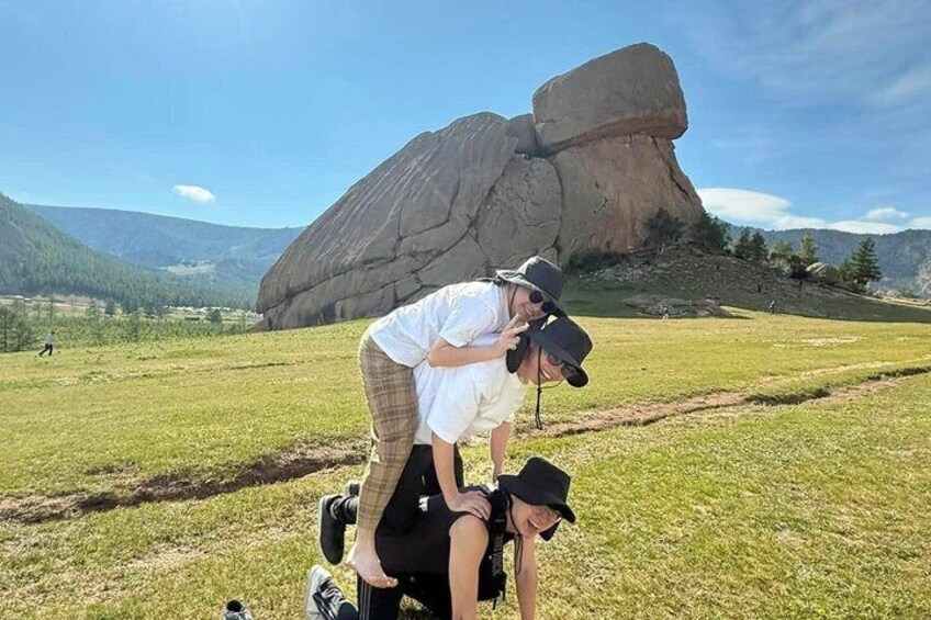 A person riding a horse in a grassy field with a large rock formation in the background. 1