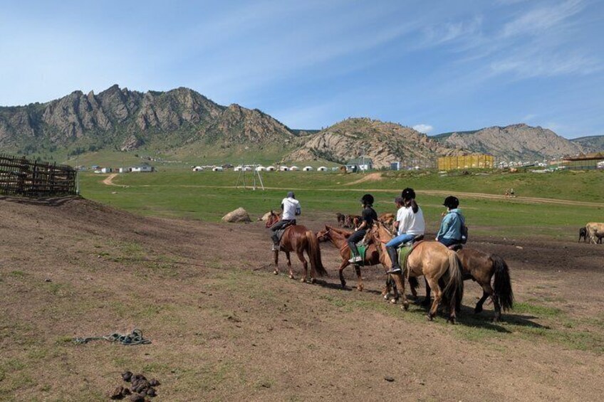 A group of people riding horses on a dirt path with mountains in the background. 4