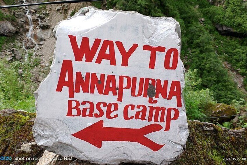 A white rock with red text and an arrow pointing left, indicating the way to Annapurna Base Camp. 5